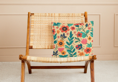 Faux suede pillow with mid century boho inspired floral reds, greens and pinks design on a rattan chair