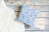 White 100% Polyester Throw pillow with blue scribbled leaves design on a wooden floor background and white fur rug